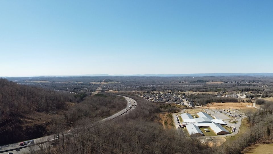 A valley with a road, buildings, and a forested hill.