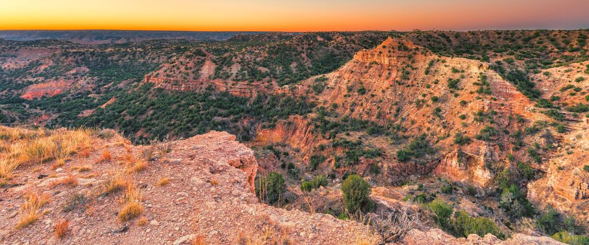 A rugged mountain landscape with sparse vegetation and a clear sky at sunset.