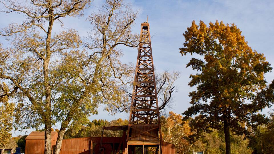 A tall metal tower with a wooden structure at its base, surrounded by autumn-colored trees.