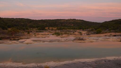 Pink and orange sky reflects on water during sunset at Pedernales Falls State Park, Texas