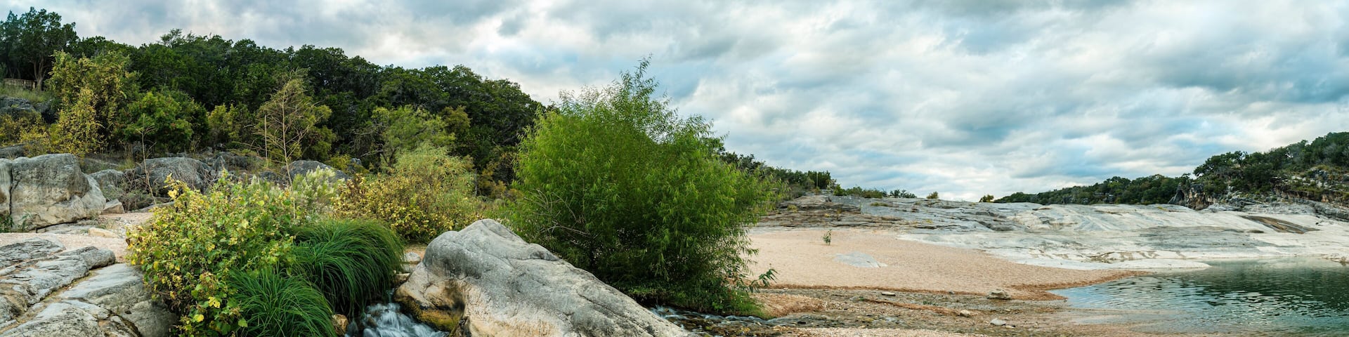 A river flowing through a rocky landscape with a sandy beach and dense forest in the background.