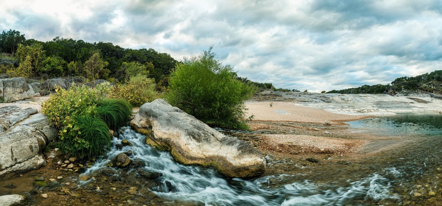A river flowing through a rocky landscape with a sandy beach and dense forest in the background.