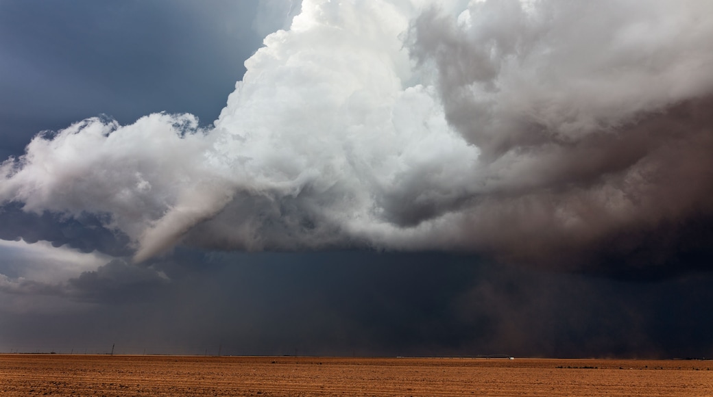 A vast, barren landscape under a dramatic sky with large, dark storm clouds.