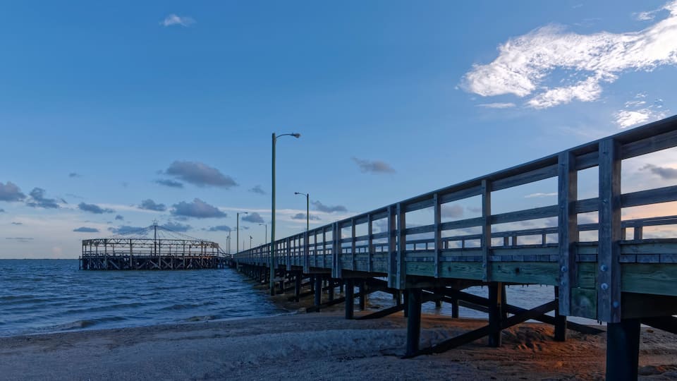 A wooden pier extending into the water with a metal structure in the distance.