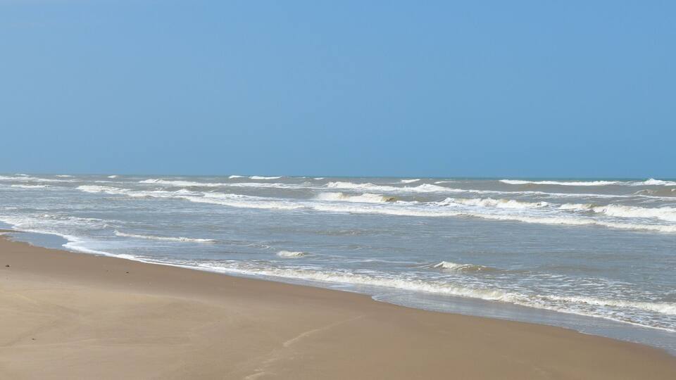 A sandy beach with waves and a clear blue sky.