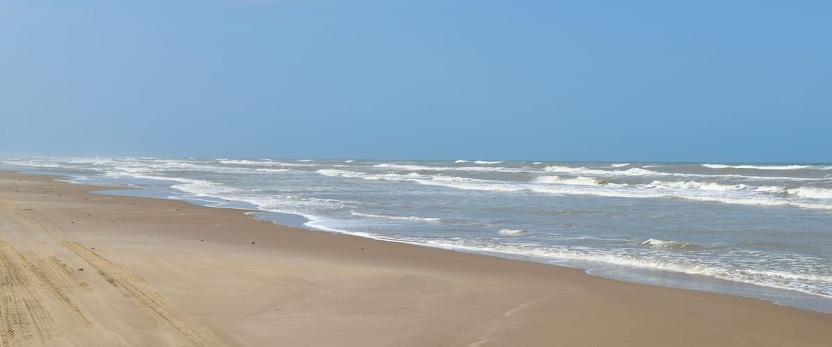 A sandy beach with waves and a clear blue sky.