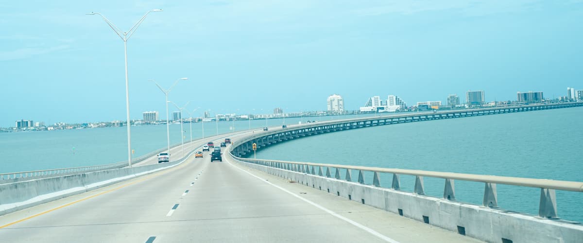 A bridge with vehicles, a waterfront, and a city skyline in the background.