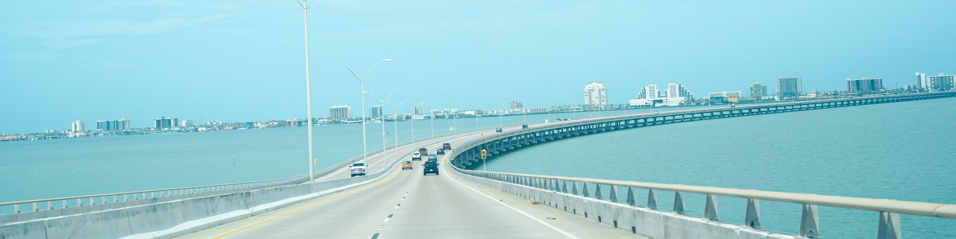 A bridge with vehicles, a waterfront, and a city skyline in the background.