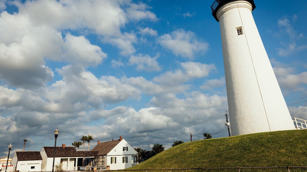 Ein weißer Leuchtturm, ein grasbewachsener Hügel und ein teilweise bewölkter Himmel.