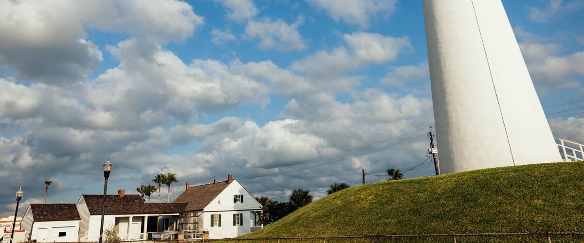 A white lighthouse, a grassy hill, and a partly cloudy sky.