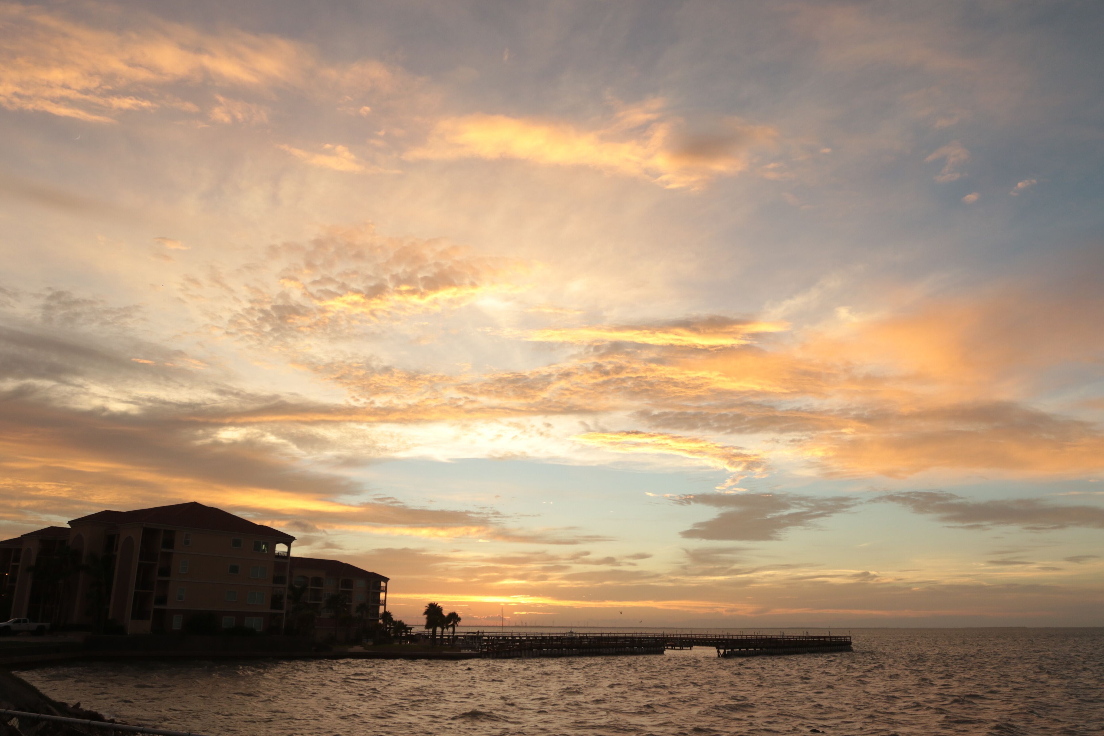 Un atardecer sobre una masa de agua con un muelle que se adentra y un edificio a la izquierda.