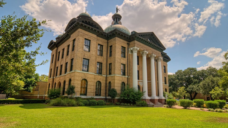 A large brick building with domed roofs and columns, surrounded by well-maintained lawns and trees.