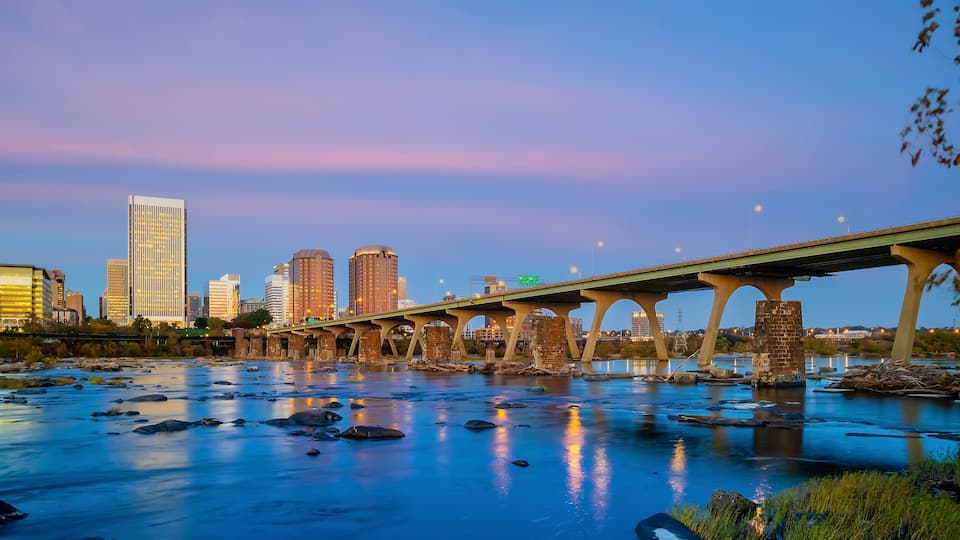 A river with rocks, a bridge, and a city skyline with tall buildings.