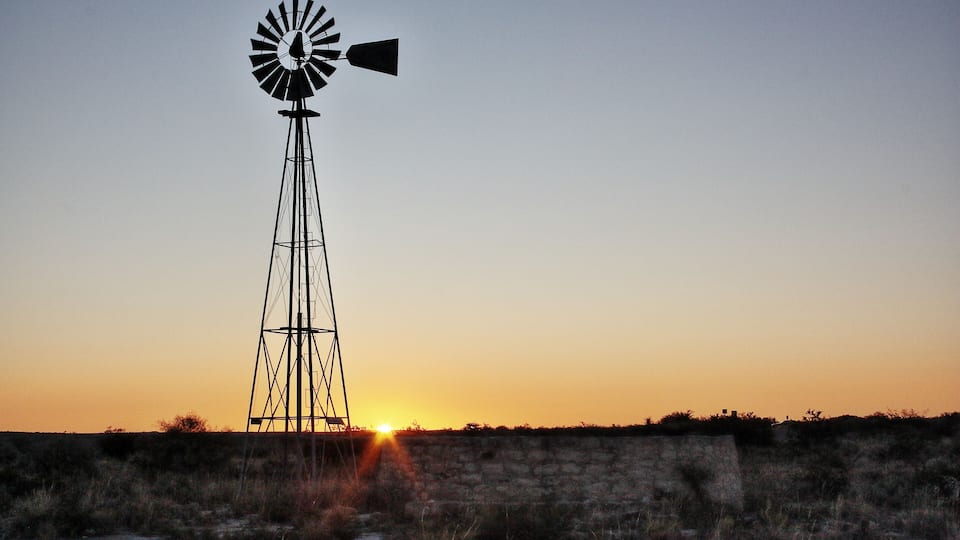 A windmill silhouetted against a sunset with the sun setting behind it.