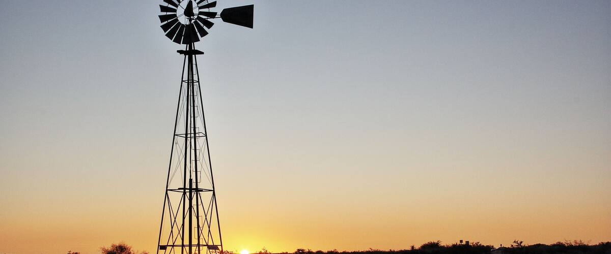 A windmill silhouetted against a sunset with the sun setting behind it.