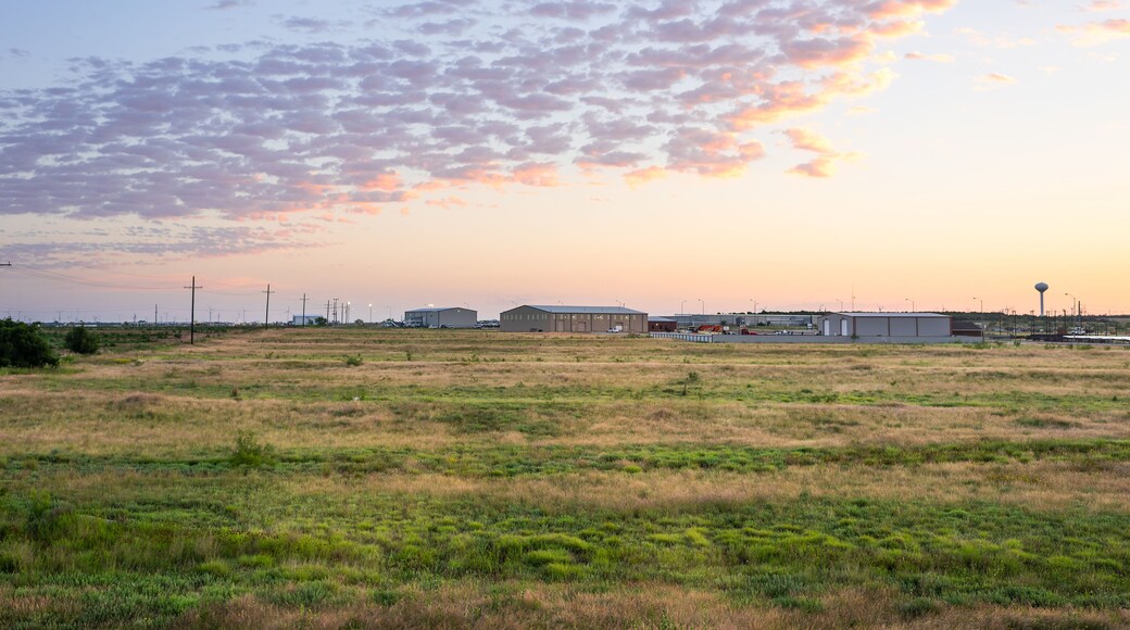 Colorful sunrise in Snyder Texas with industrial building, warehouses or storehouses and factory by farm field with electricity pylons