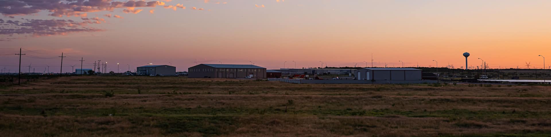 Colorful dark dawn sunrise in Snyder Texas with industrial building, warehouses or storehouses and factory by farm field with electricity pylons
