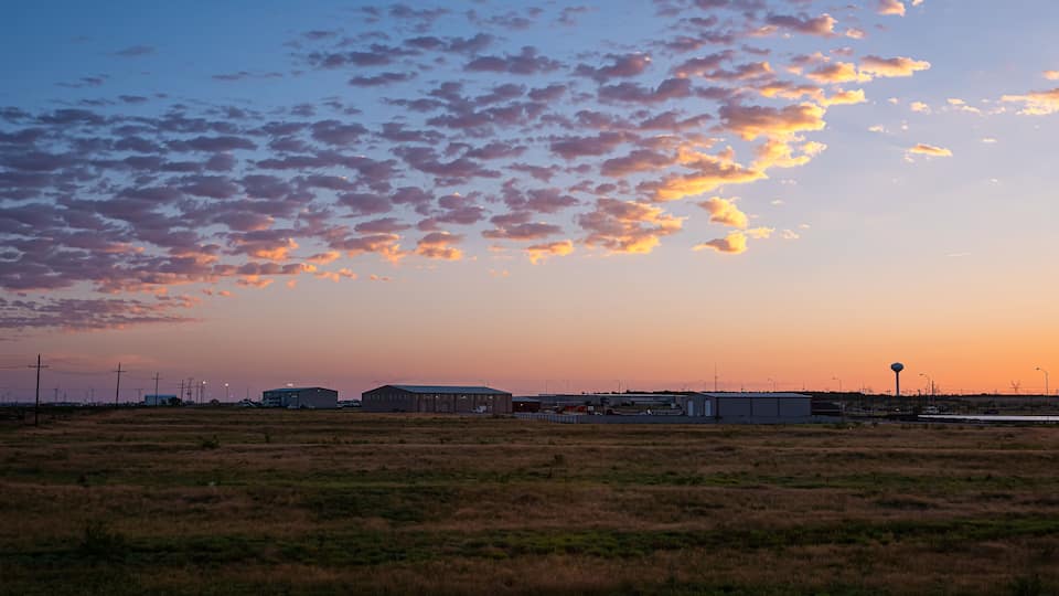 A sunset over a flat landscape with industrial buildings and wind turbines.