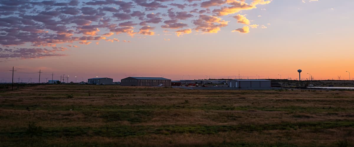 A sunset over a flat landscape with industrial buildings and wind turbines.