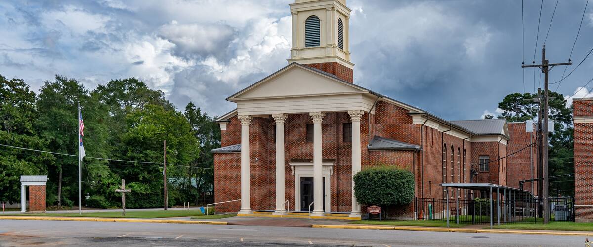 A brick church with a tall steeple and a flagpole.