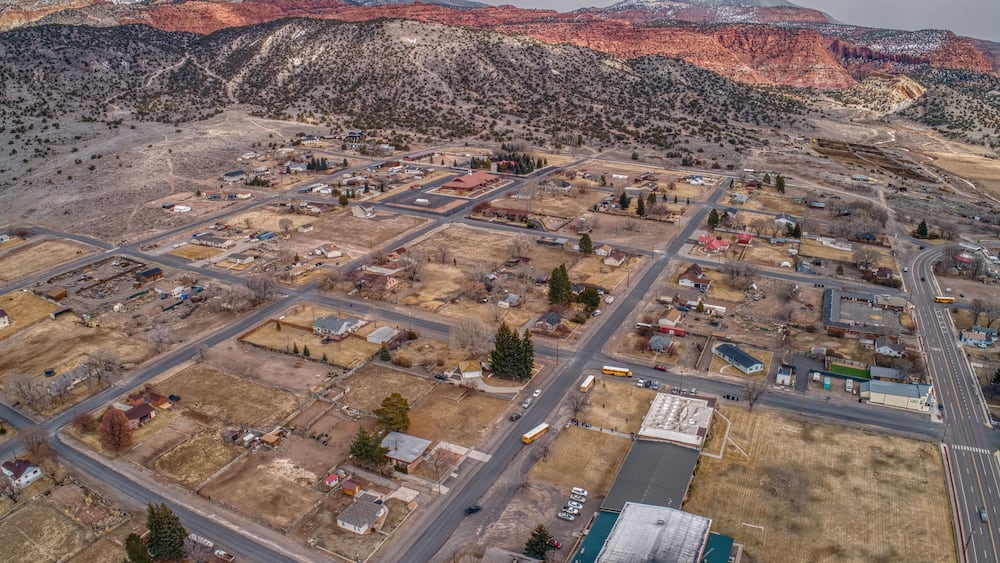 An aerial view of a town with a grid of streets, surrounded by mountains and sparse vegetation.