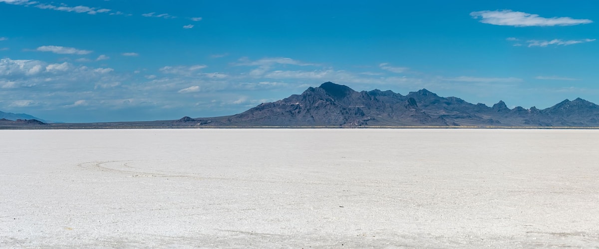 A vast salt flat with distant mountain ranges under a clear blue sky.