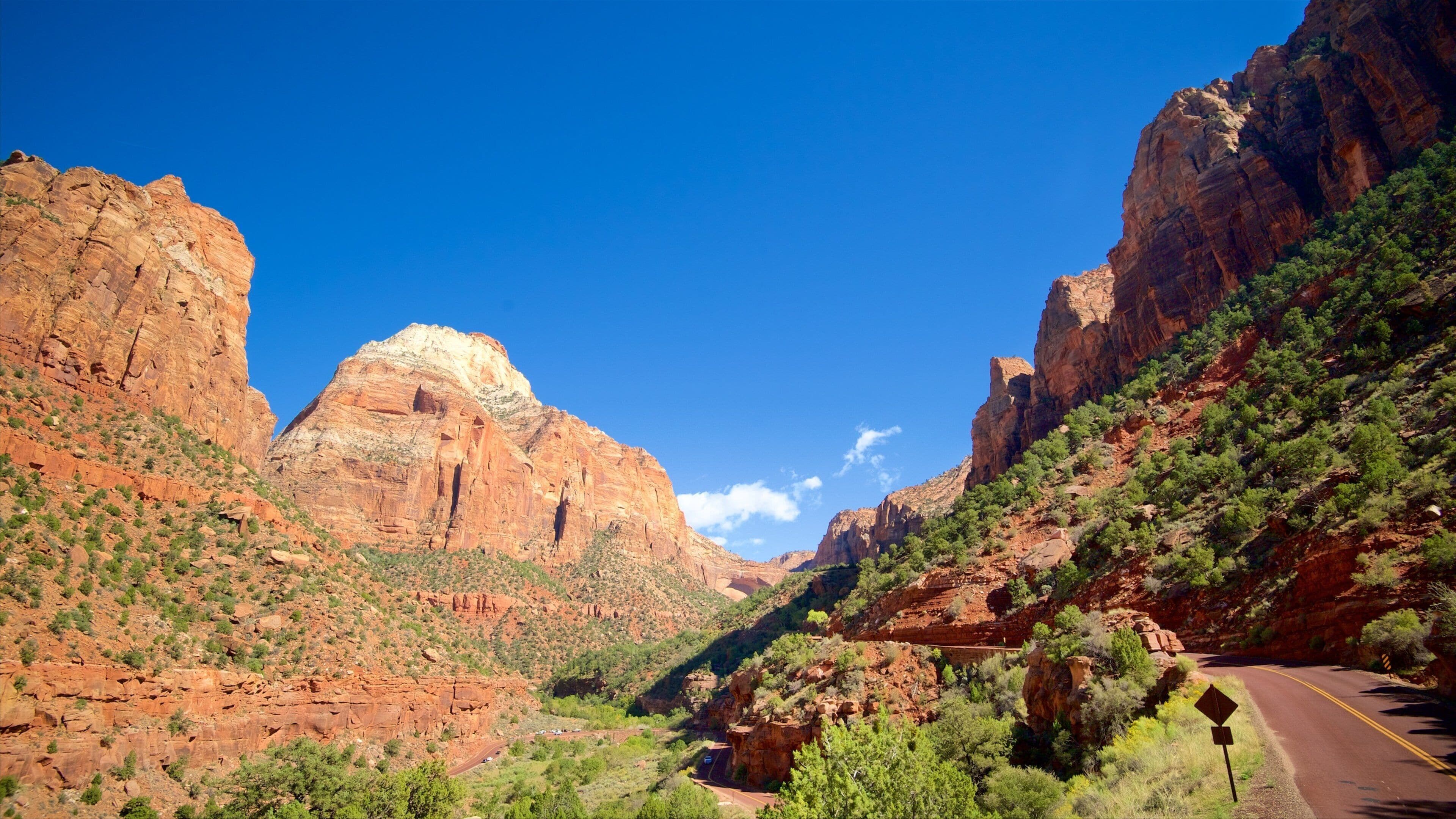 A canyon with a prominent rock formation, a winding road, and sparse vegetation.