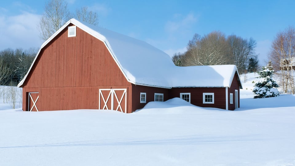 A red barn with a snow-covered roof in a snowy landscape.