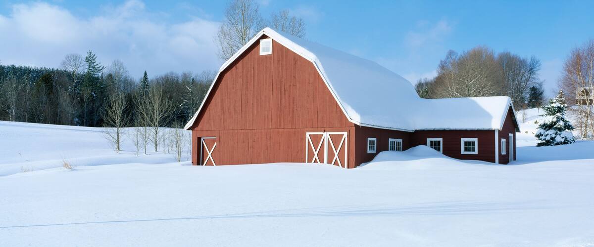 A red barn with a snow-covered roof in a snowy landscape.