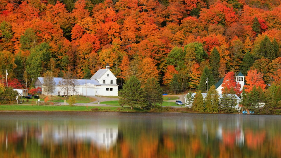 A white house surrounded by autumn foliage and a calm lake.