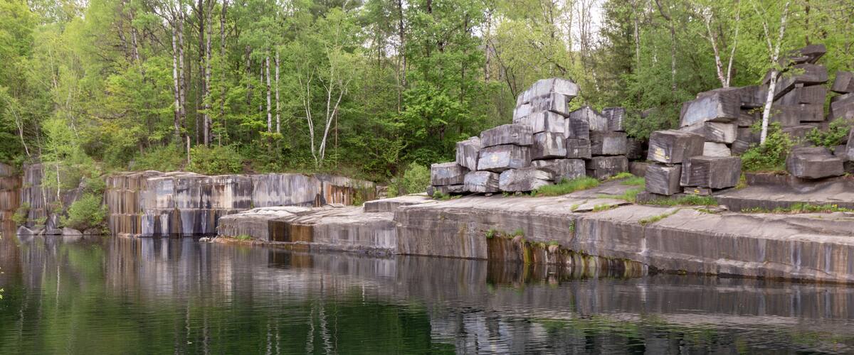 A calm river with rocky formations and dense green trees in the background.