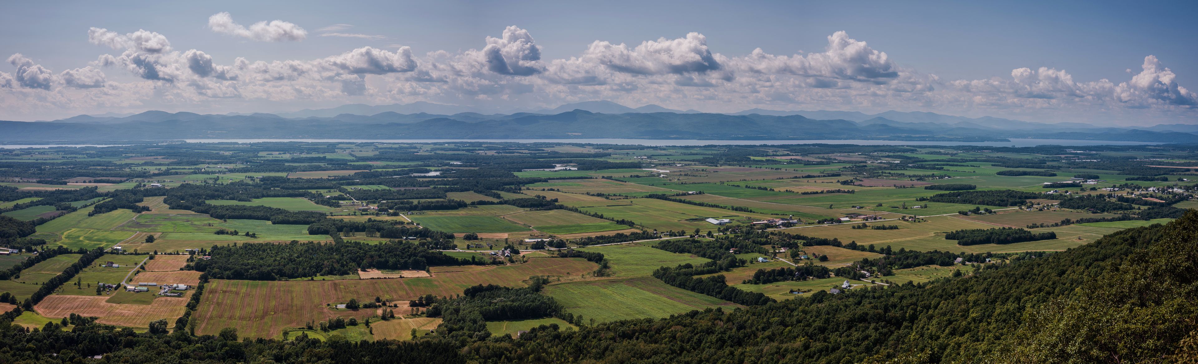 A panoramic view of a valley with fields, scattered houses, and mountains in the distance.