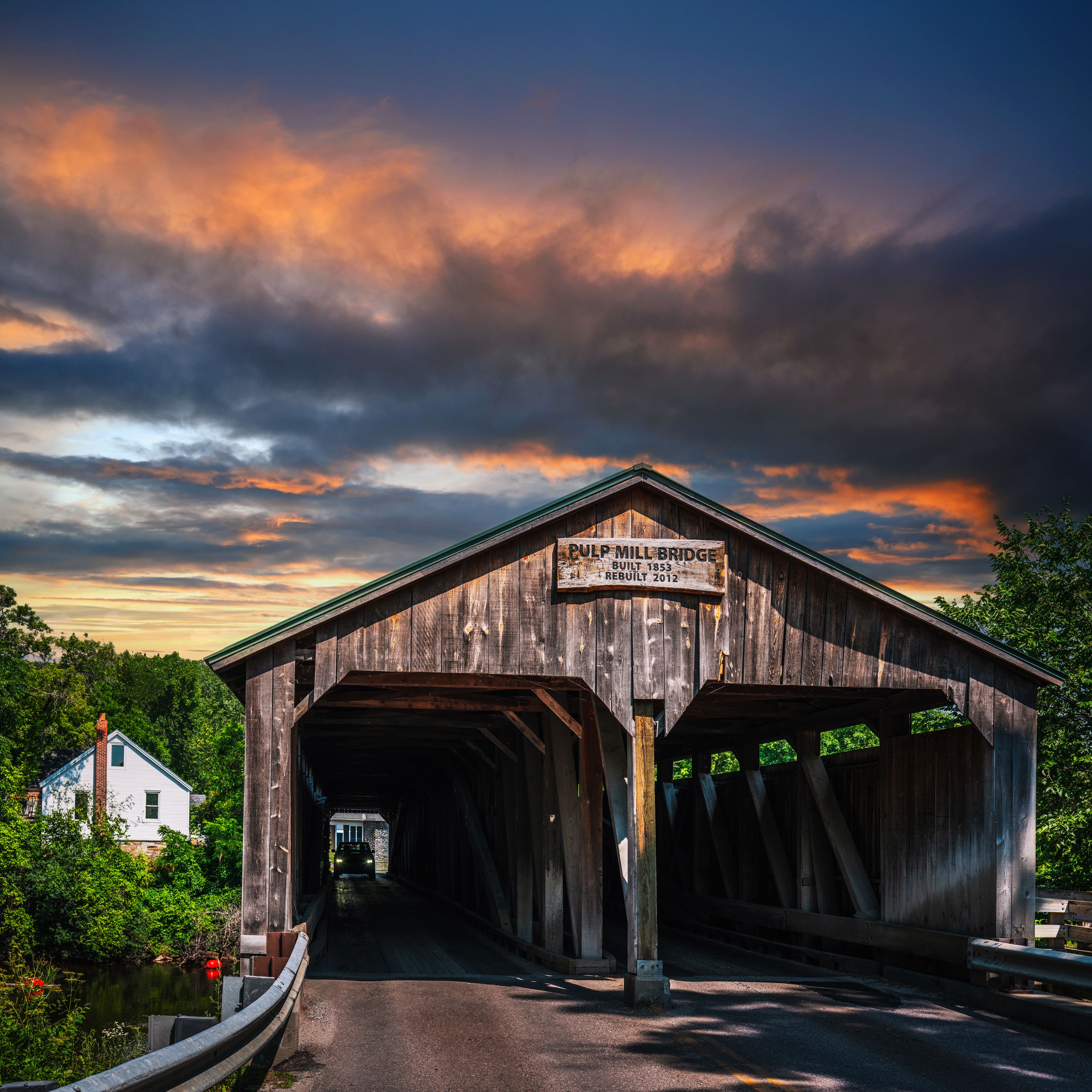 A covered wooden bridge with a sign reading 'Pulp Mill Bridge Built 1853 Rebuilt 2012.'