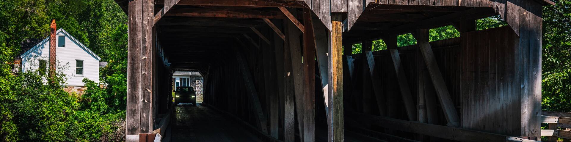 A covered wooden bridge with a sign reading 'Pulp Mill Bridge Built 1853 Rebuilt 2012.'