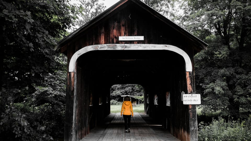 A covered wooden bridge with a sign reading "McWilliam Bridge" and a "NO VEHICLES FOOT PATH ONLY" sign.