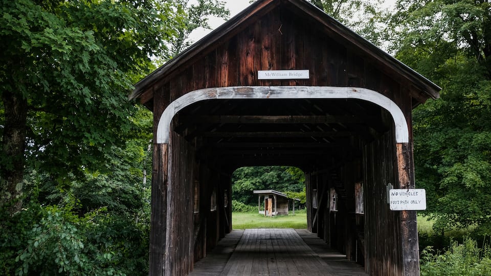 A covered wooden bridge named McWilliam Bridge with a 'No Vehicles, Foot Path Only' sign.