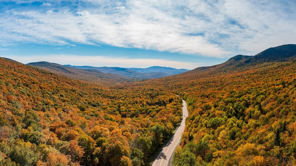 A road through a forested valley with autumn foliage.