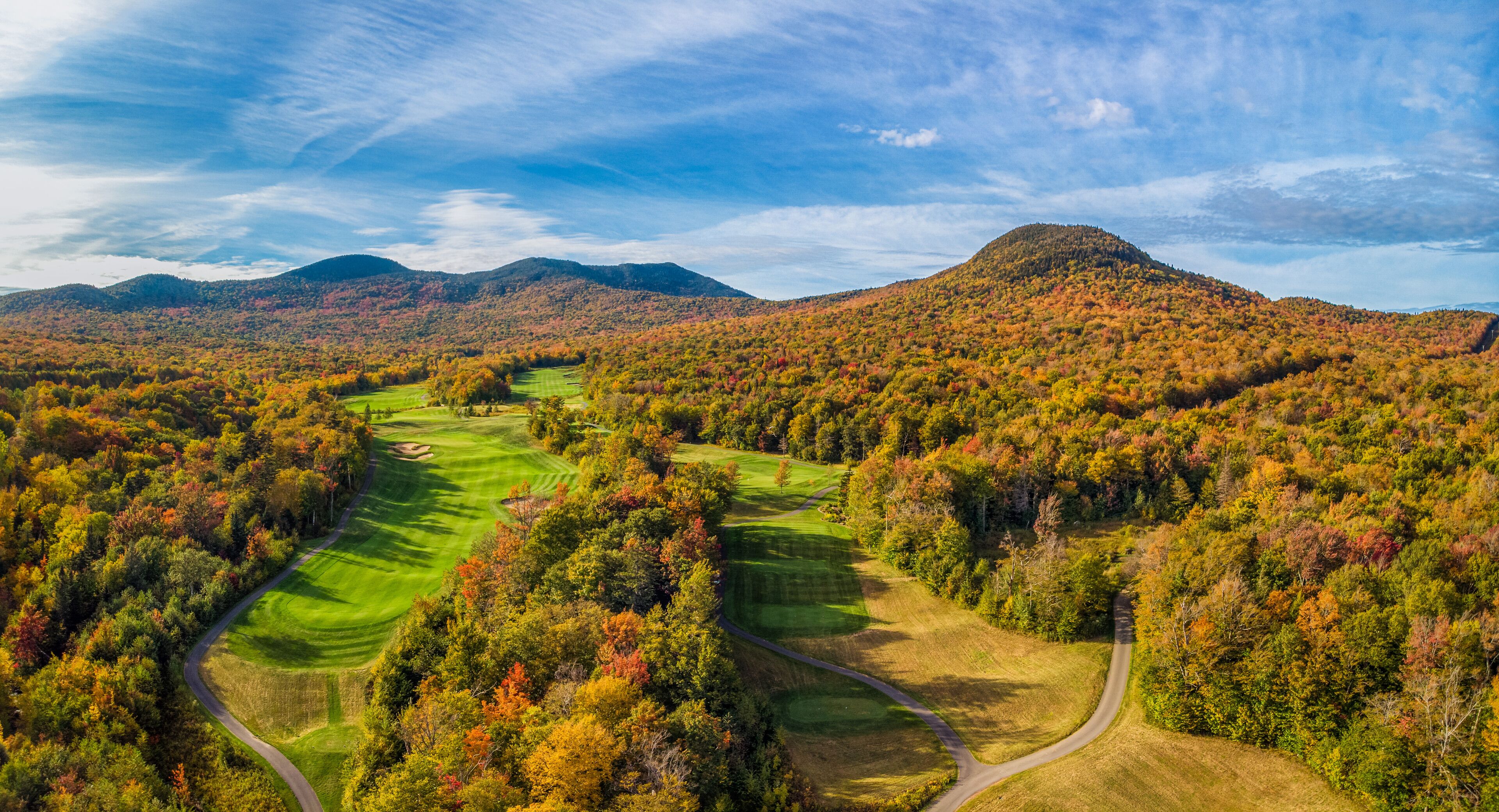 A golf course surrounded by autumn-colored trees and mountains.