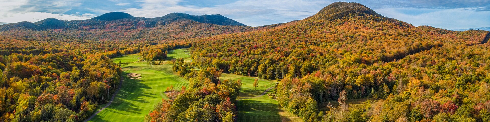 A golf course surrounded by autumn-colored trees and mountains.