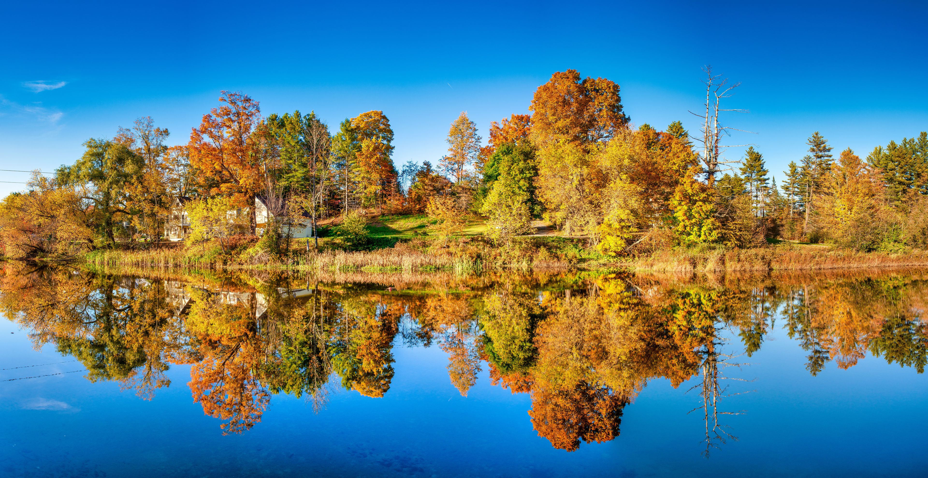 A calm lake reflecting autumn trees and a clear blue sky.