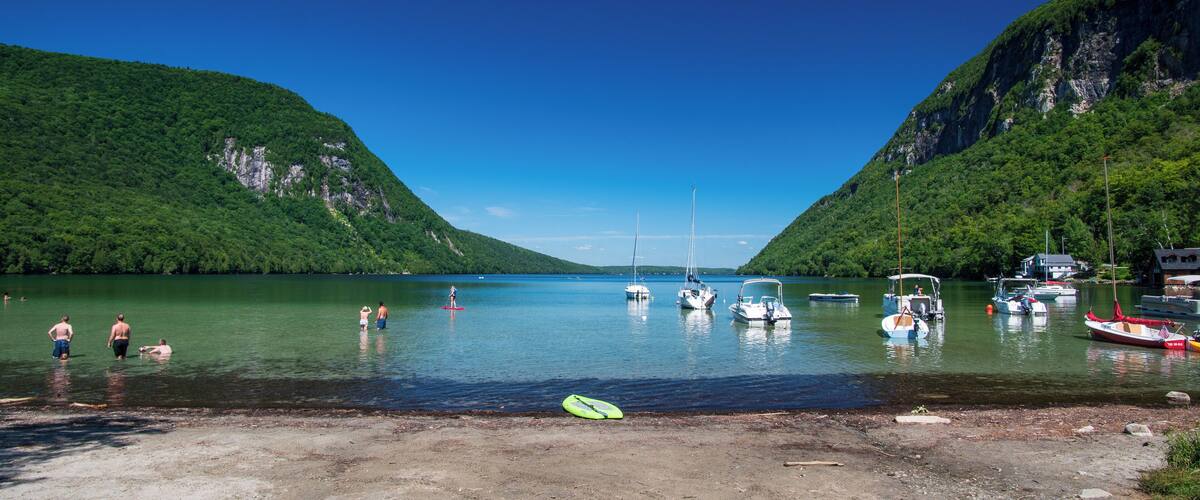 A lake surrounded by mountains with boats and people on the shore.