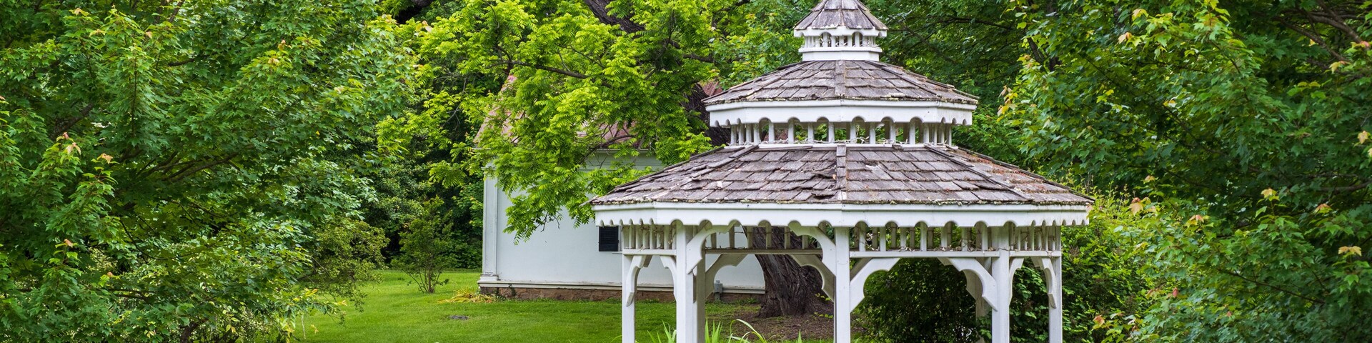 Um gazebo branco rodeado por árvores e grama verdejantes.
