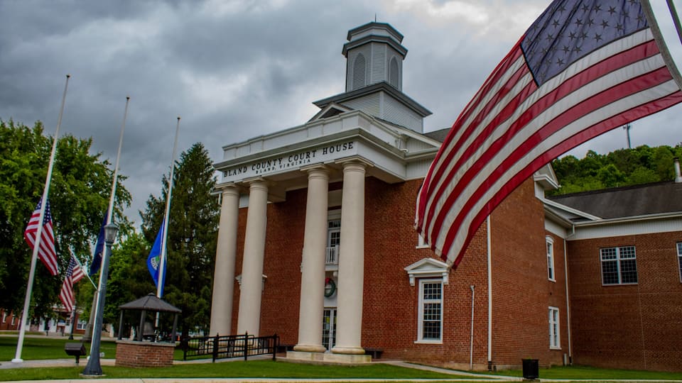 A brick courthouse with columns and a flagpole with multiple flags.
