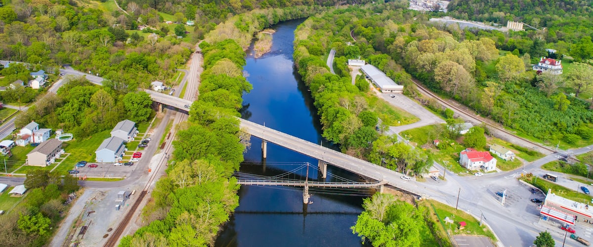 A river flowing through a valley with a bridge, surrounded by green hills and buildings.