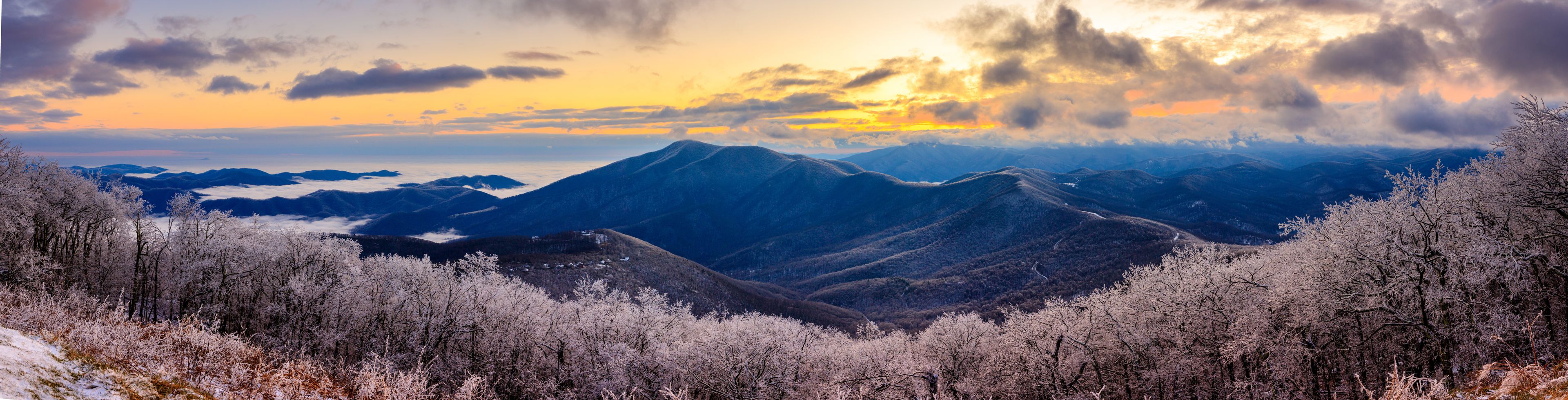 Paesaggio montuoso con alberi innevati e un tramonto.