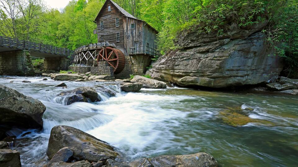 A wooden mill with a water wheel, a river, and a bridge.