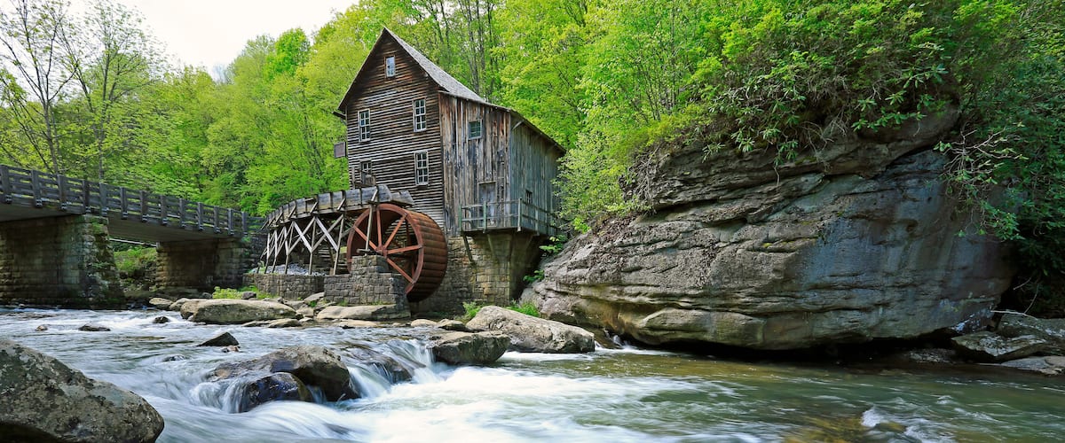 A wooden mill with a water wheel, a river, and a bridge.
