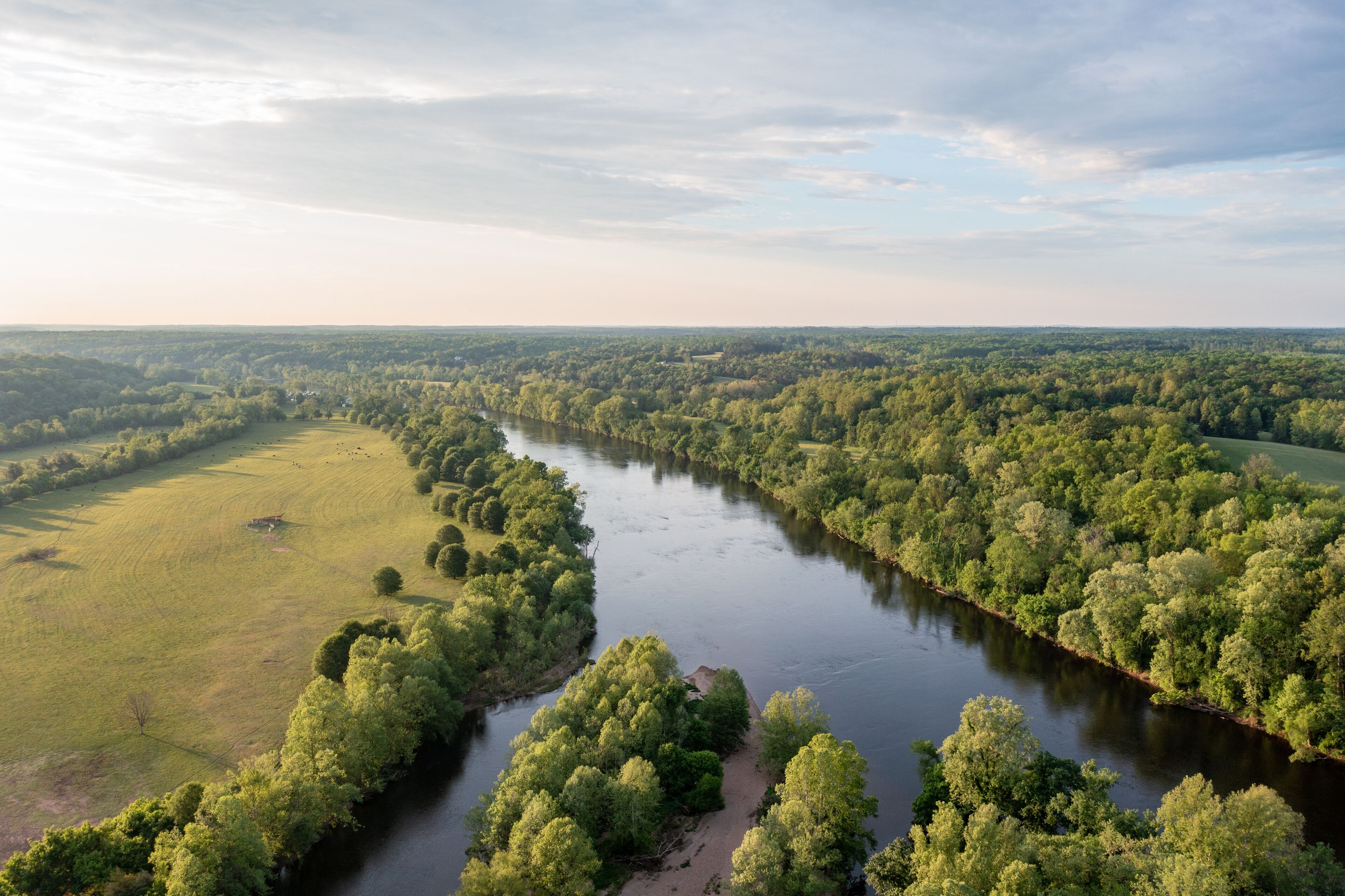 A river winding through a densely forested landscape with open fields on either side.