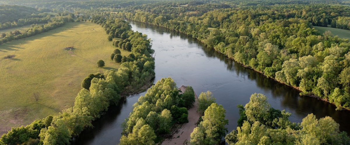 A river winding through a densely forested landscape with open fields on either side.