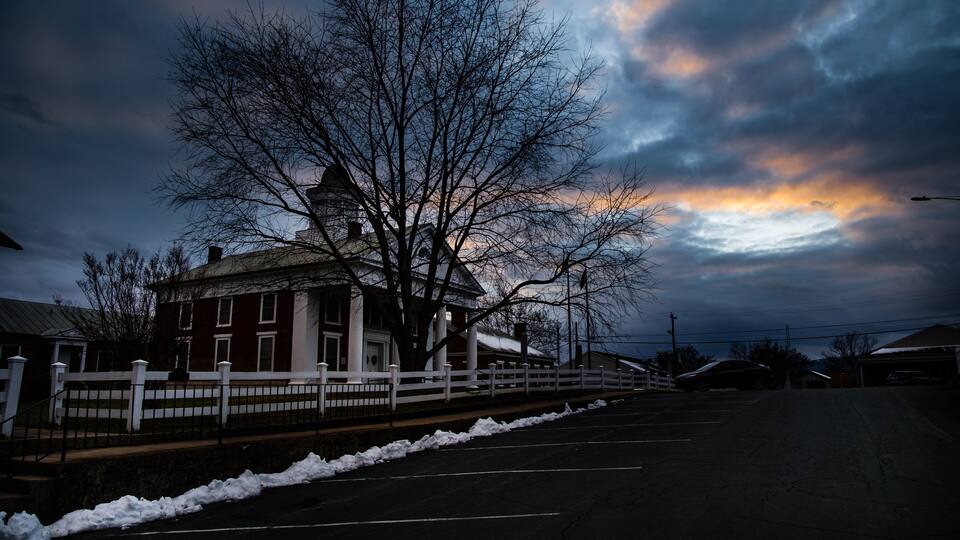 A building with a white fence, a tree, and a cloudy sky.